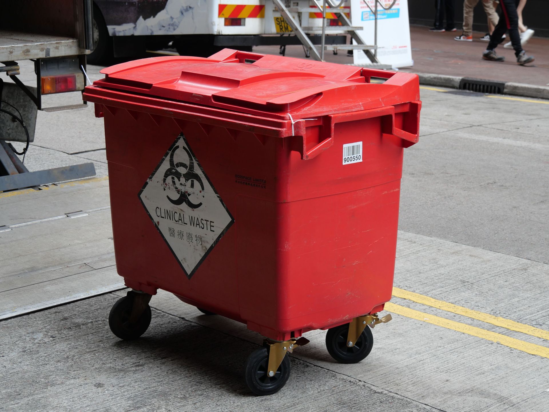 A red clinical waste bin labeled with biohazard symbol on a city street indicating proper waste management.